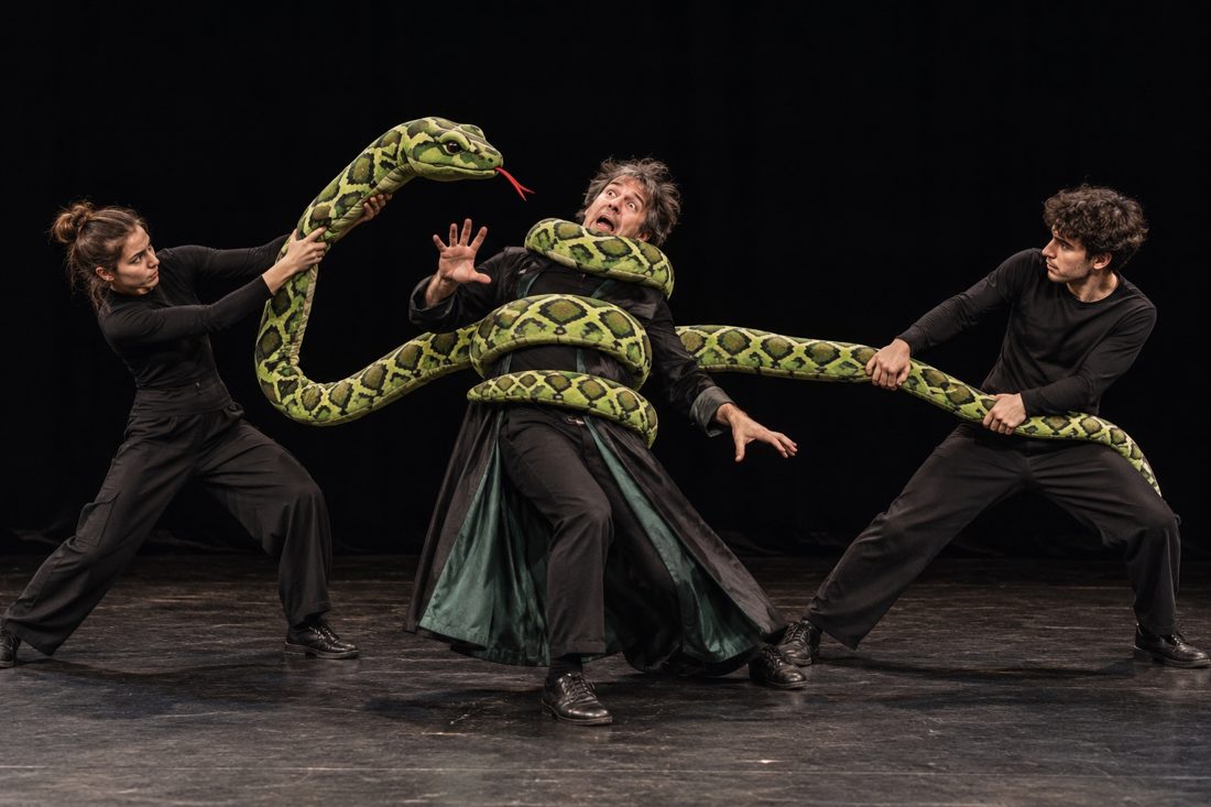 Two actors manipulate a giant snake puppet wrapped around Mortimer on stage